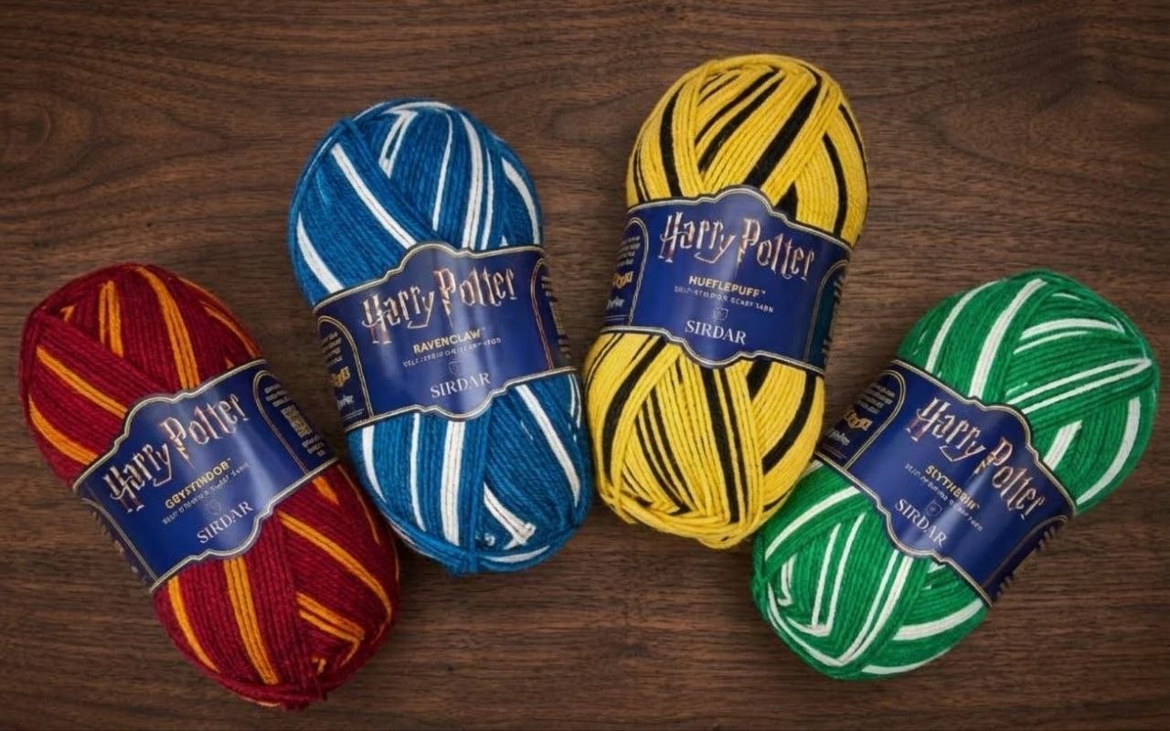 Four balls of Sirdar Harry Potter scarf wool in Gryffindor red and gold, Ravenclaw blue and white, Hufflepuff yellow and black, and Slytherin green and white